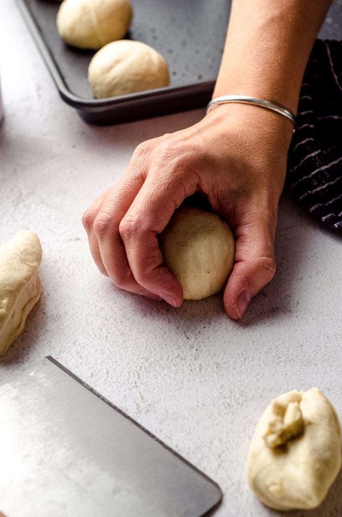 A hand hold a portion of sourdough roll dough to make a ball.