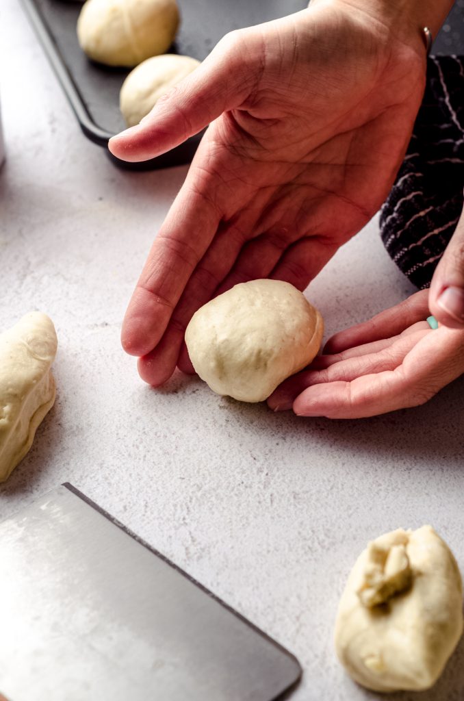 A hand hold a portion of sourdough roll dough to make a ball.