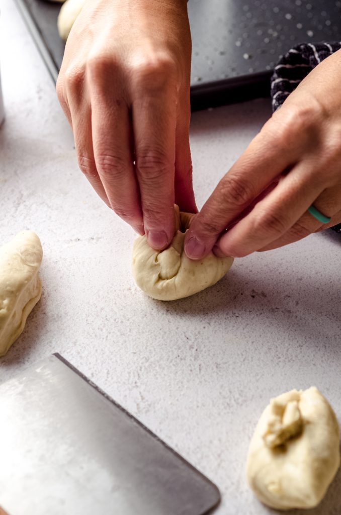 A hand pressing a portion of sourdough roll dough to make a ball.