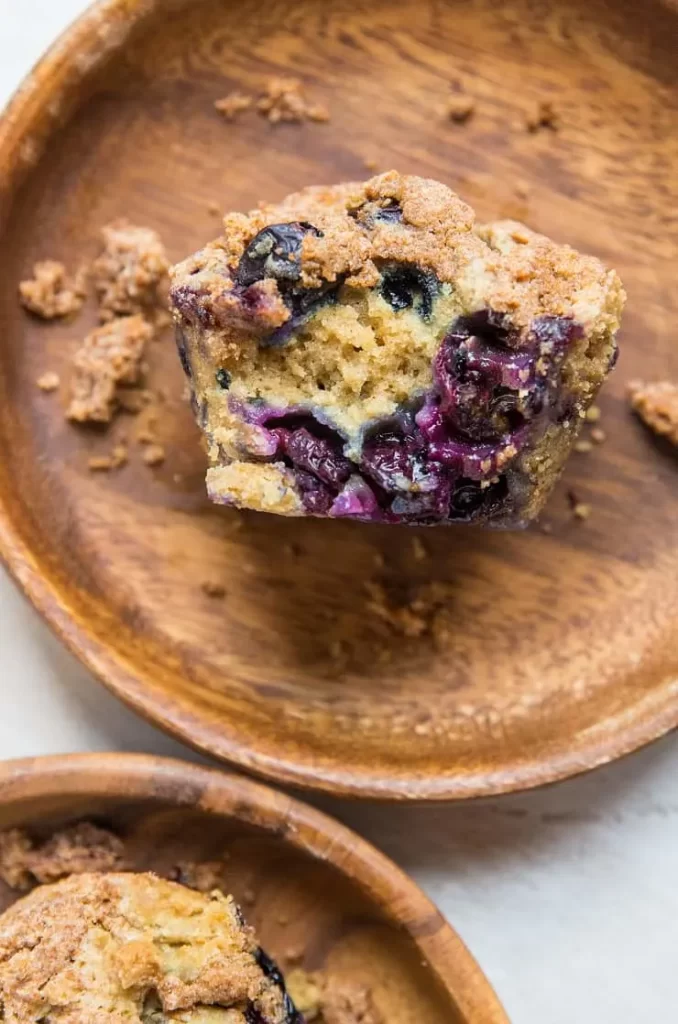 A blueberry sourdough muffin with a bite taken from it lying on a surface.