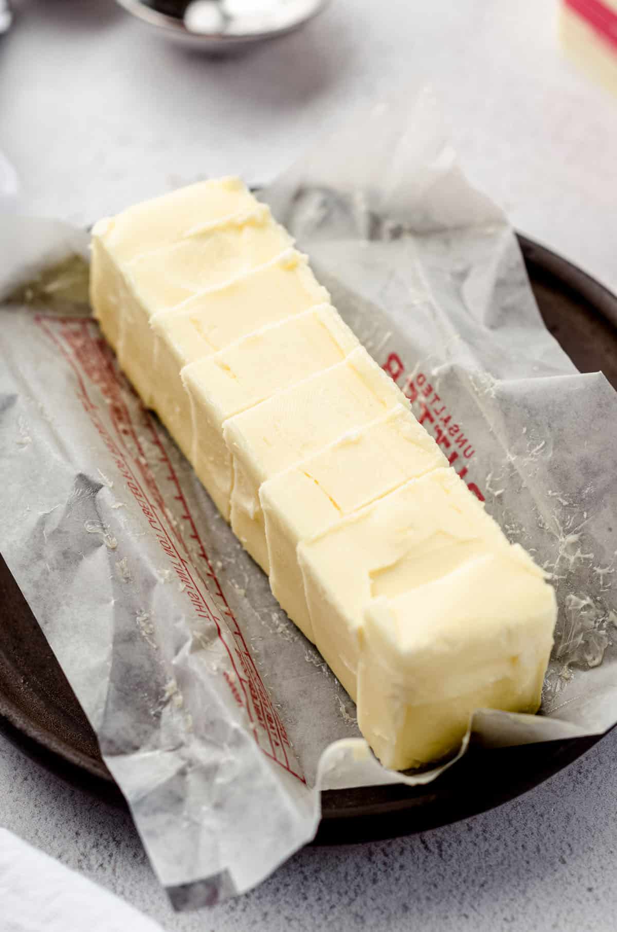 A stick of butter sliced and on its wrapper on a plate.