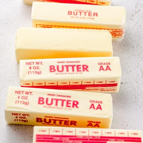 Several sticks of butter in the wrapper and one that has been unwrapped.