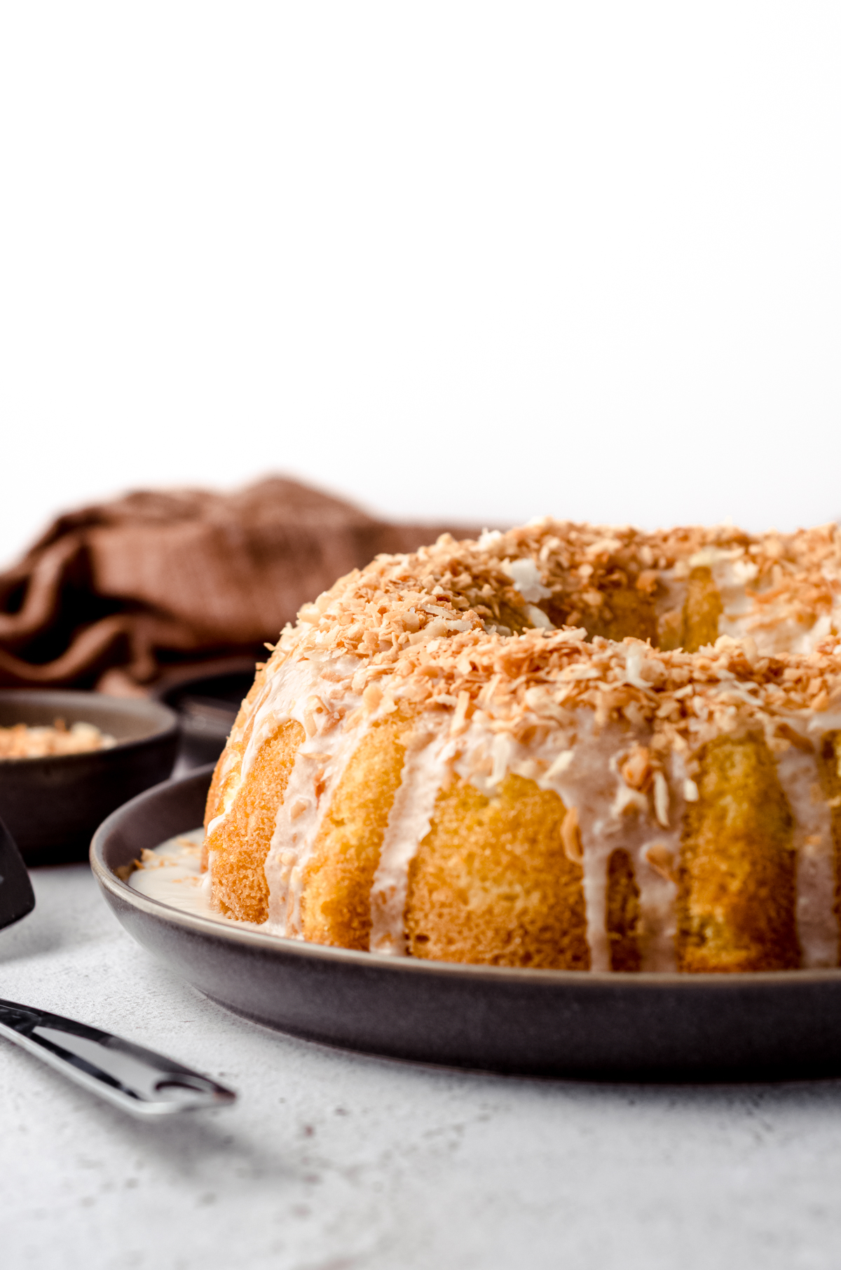 side view of coconut bundt cake on a serving platter with bowl of coconut in the background.