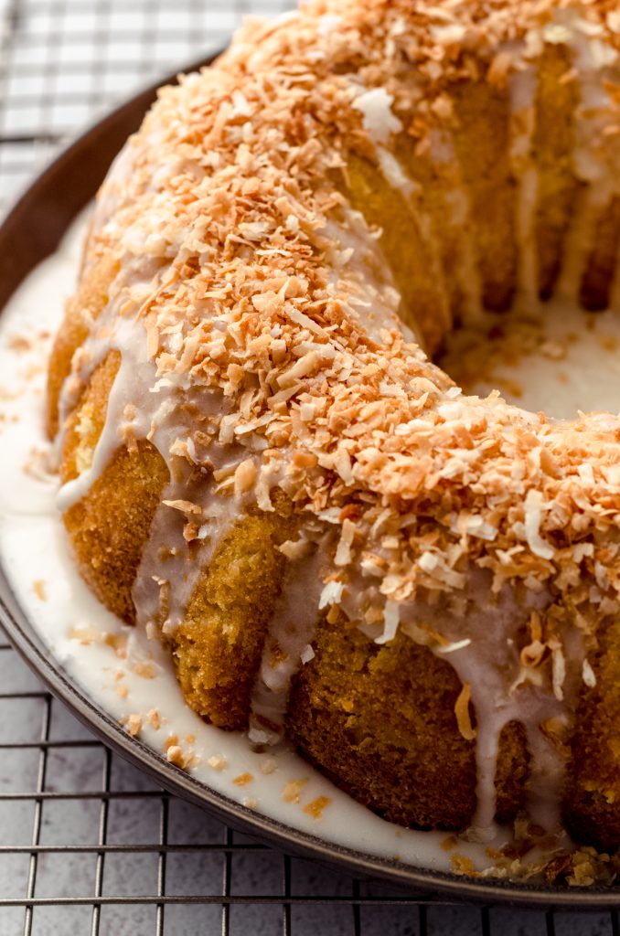 Close up view of coconut bundt cake on serving platter with glaze and coconut on top.