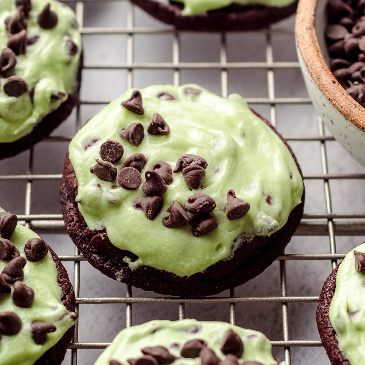 Mint chocolate chip cookie on a cooling rack with mini chocolate chips sprinkled on top. 