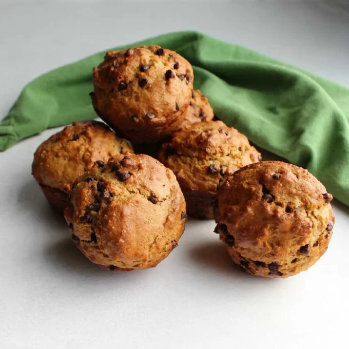 Oatmeal chocolate chip sourdough muffins in a surface with a green kitchen towel in the background.