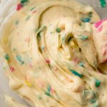 A bowl of homemade rainbow chip frosting with a spatula in it.
