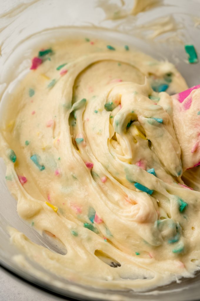 A bowl of homemade rainbow chip frosting with a spatula in it.
