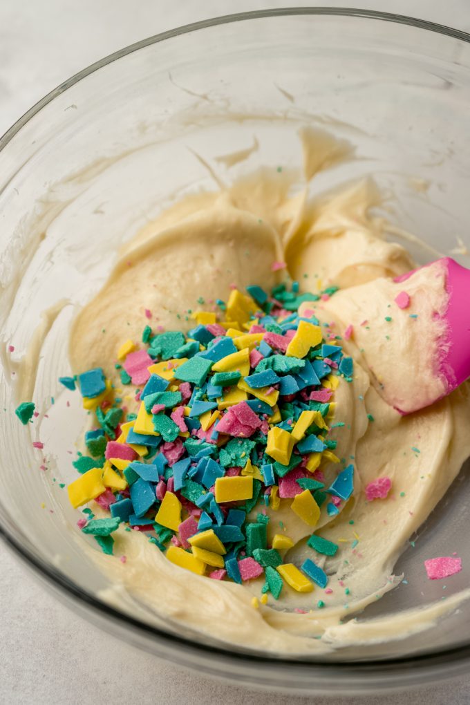 A bowl of homemade rainbow chip frosting with a spatula in it.