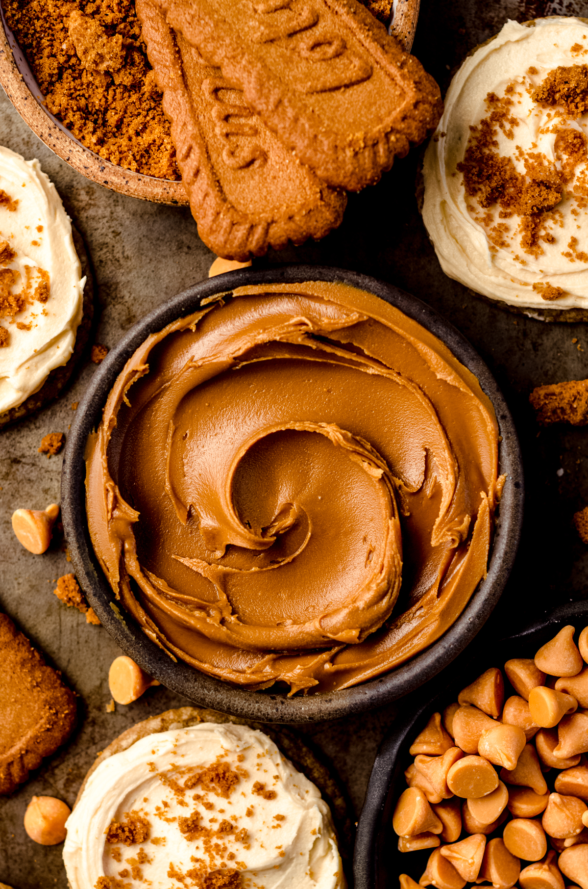 An aerial photo of Biscoff cookie butter spread in a bowl surrounded by cookies and butterscotch chips.