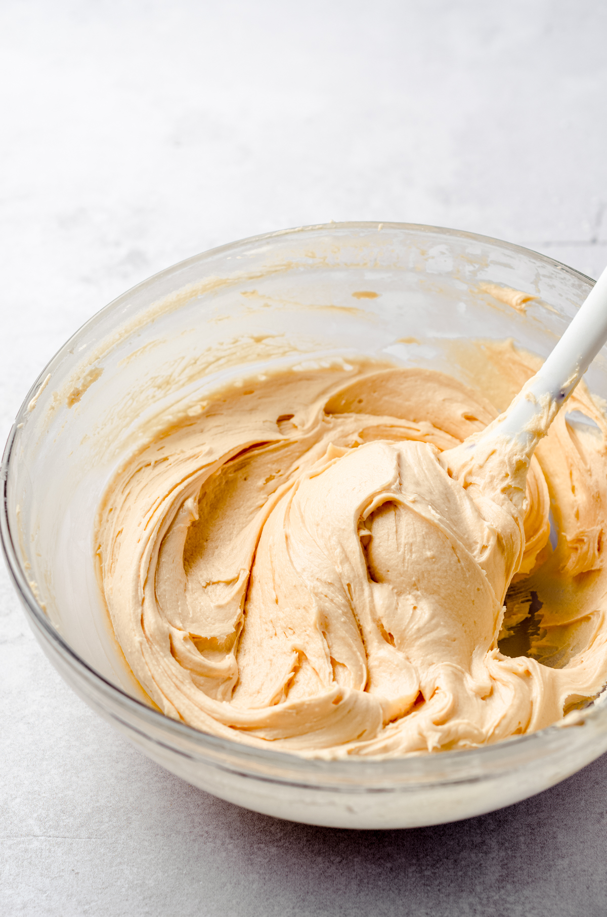 A bowl of butterscotch frosting in a glass bowl with a spatula.