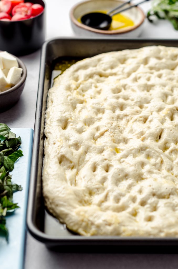 Dimpled focaccia dough in a baking dish.