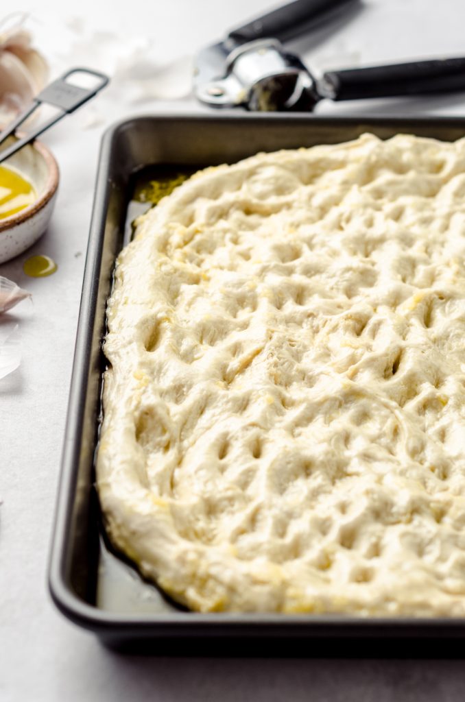 Dimpled dough for focaccia ready to rise in a baking dish.