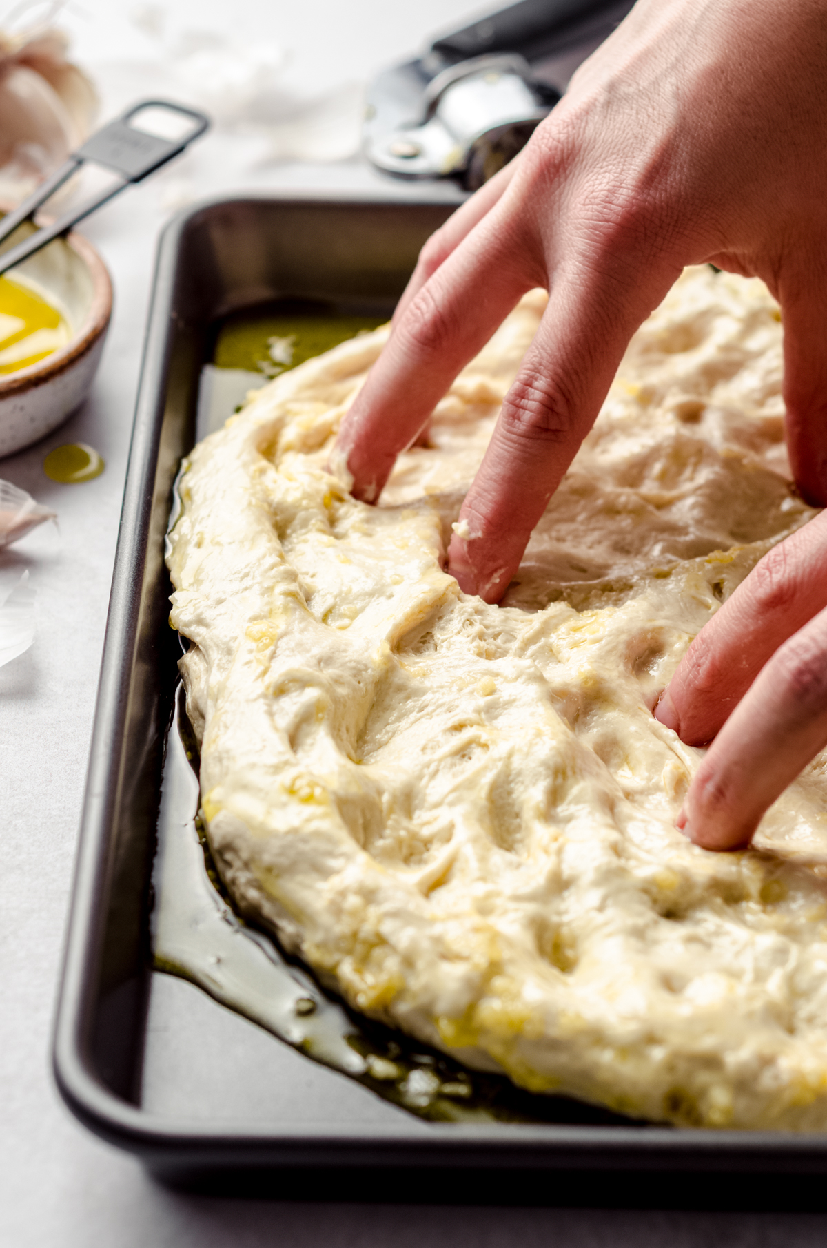 Someone is using their fingers to dimple focaccia dough in a baking dish.