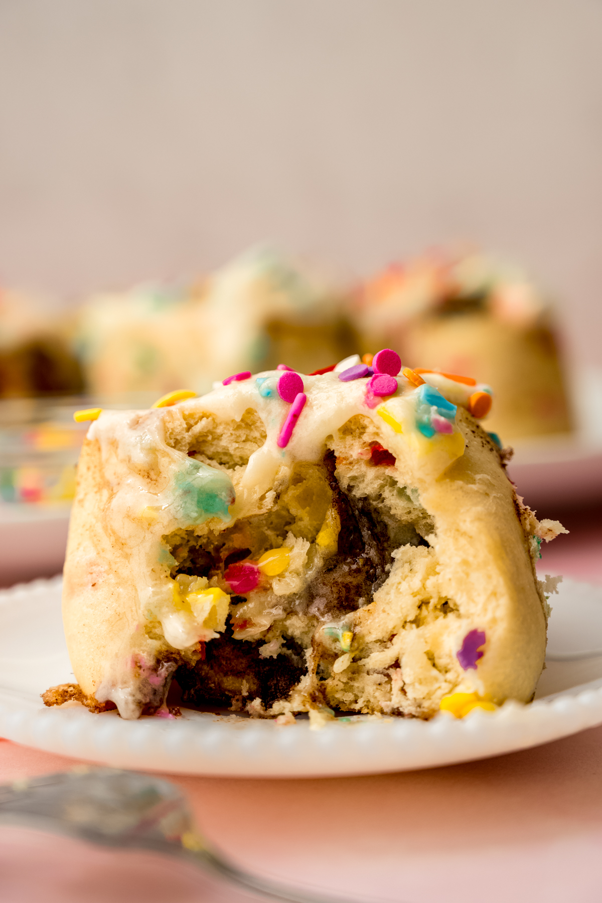 A confetti cinnamon roll on a plate and a bite has been taken out of it.