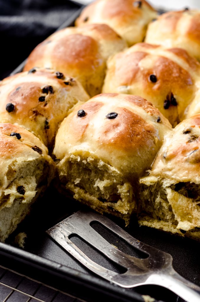 Hot cross buns in a baking dish with a serving utensil.