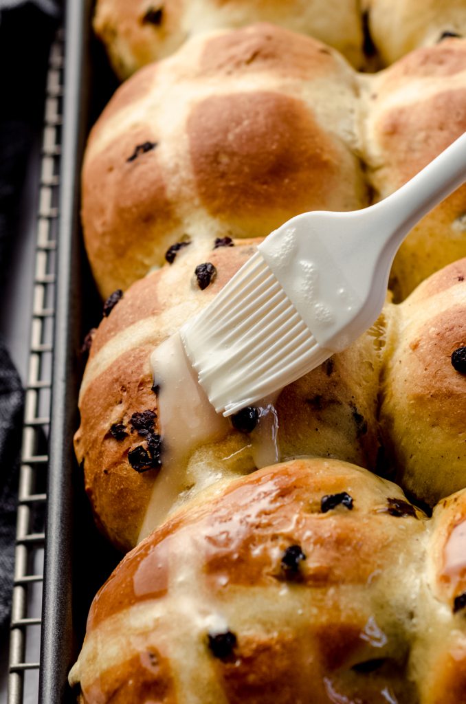 A pastry brush glazing hot cross buns with a simple vanilla glaze.