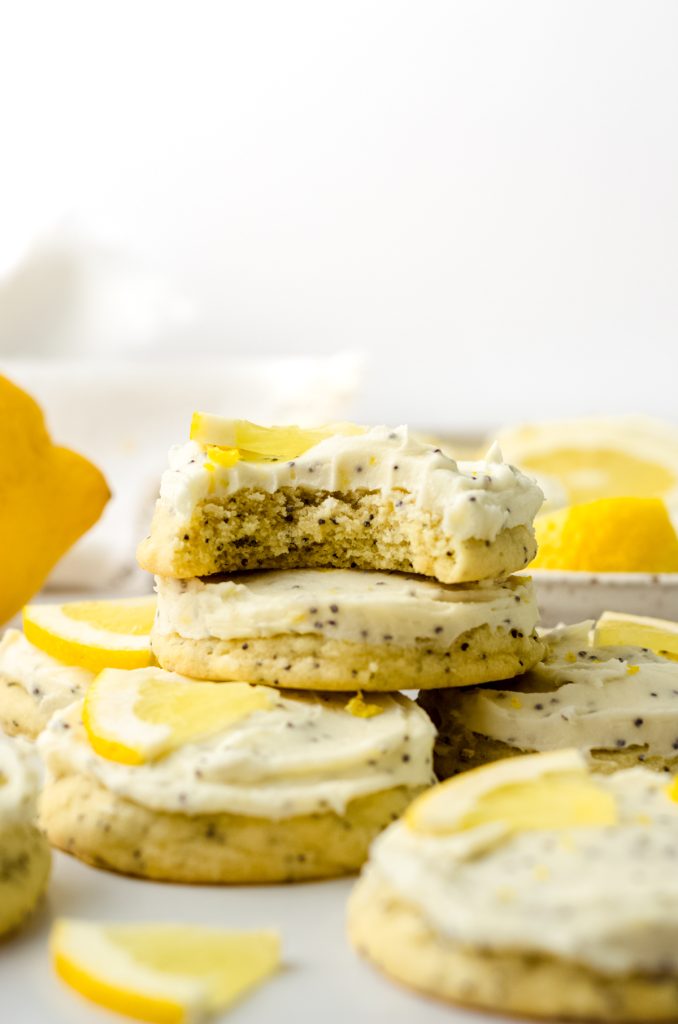 A stack of frosted lemon poppy seed cookies with a bite taken out of the one on the top.