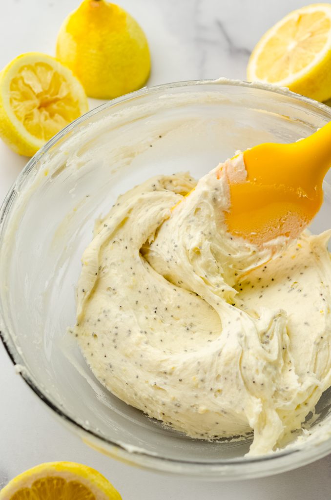 Lemon poppy seed frosting in a bowl with a yellow spatula.