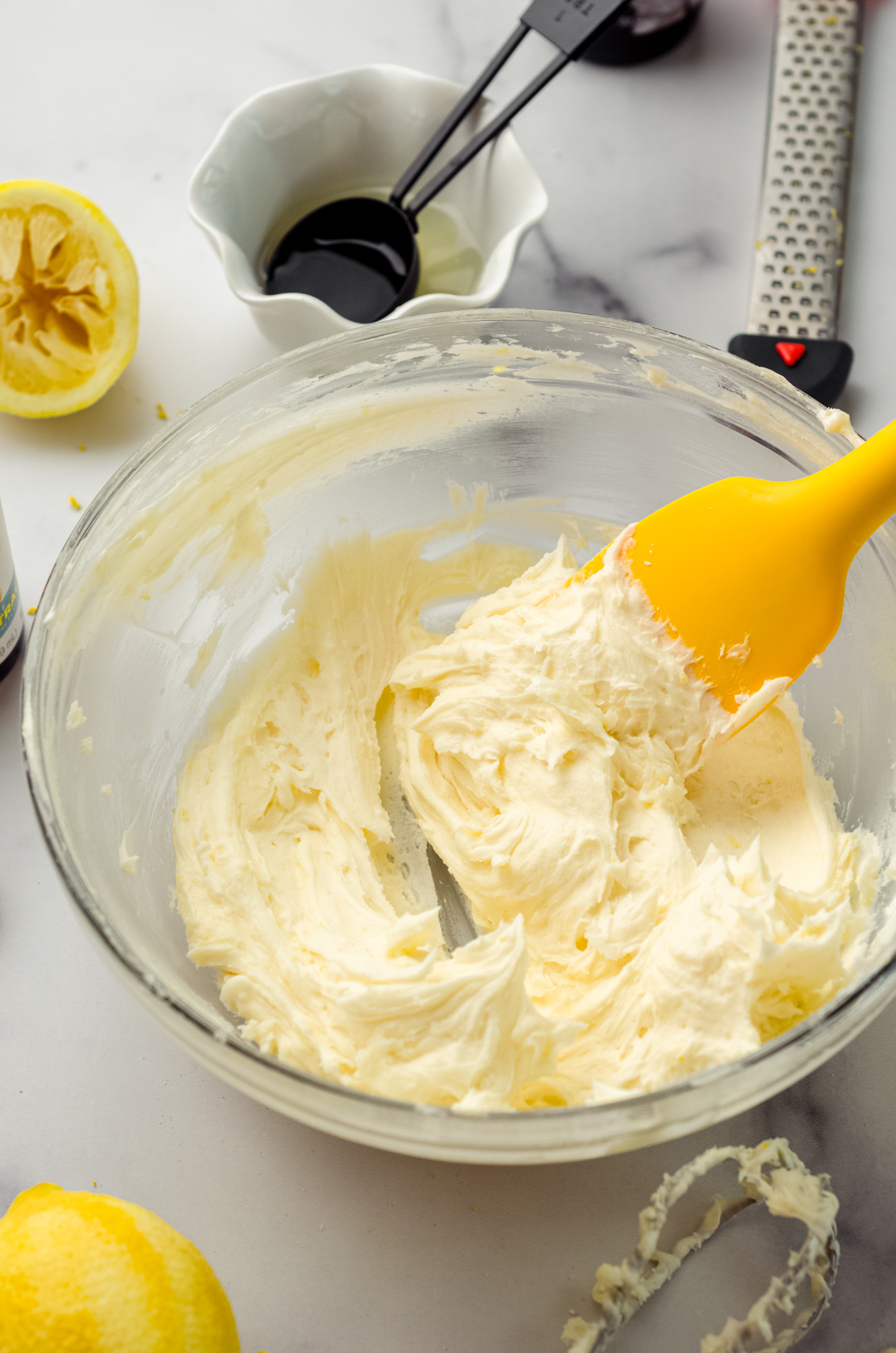 Lemon frosting in a bowl with a yellow spatula.