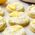 Frosted lemon poppy seed cookies with fresh lemon slices on top on a surface.