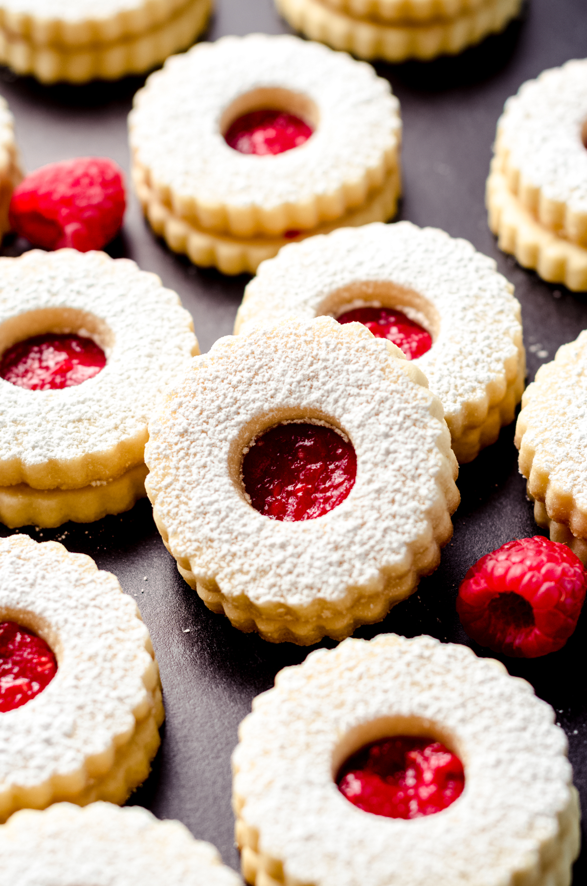 Raspberry Linzer cookies on a black surface.
