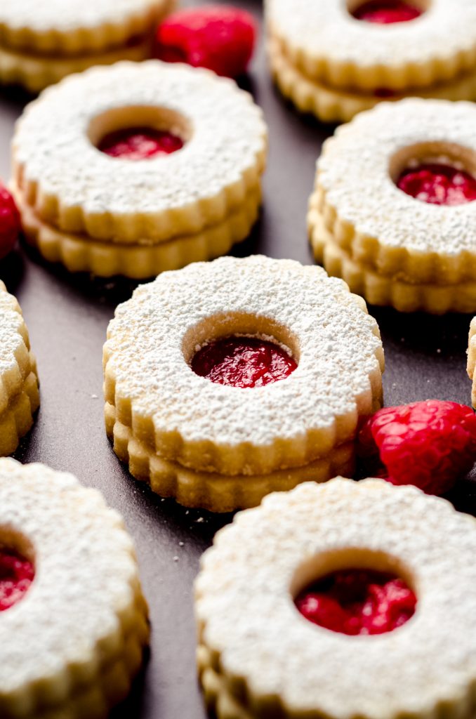Raspberry Linzer cookies on a black surface.