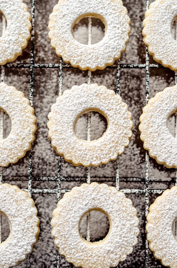 The tops of Linzer cookies on a cooling rack. They have just been dusted with powdered sugar.