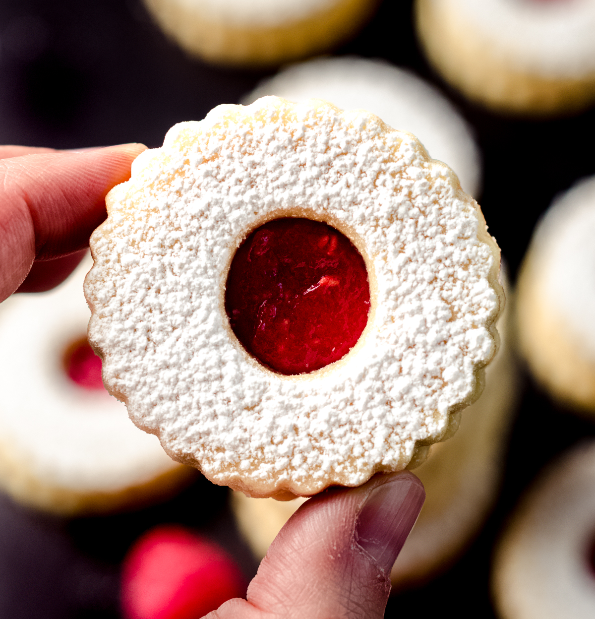 Someone is holding a raspberry Linzer cookie.