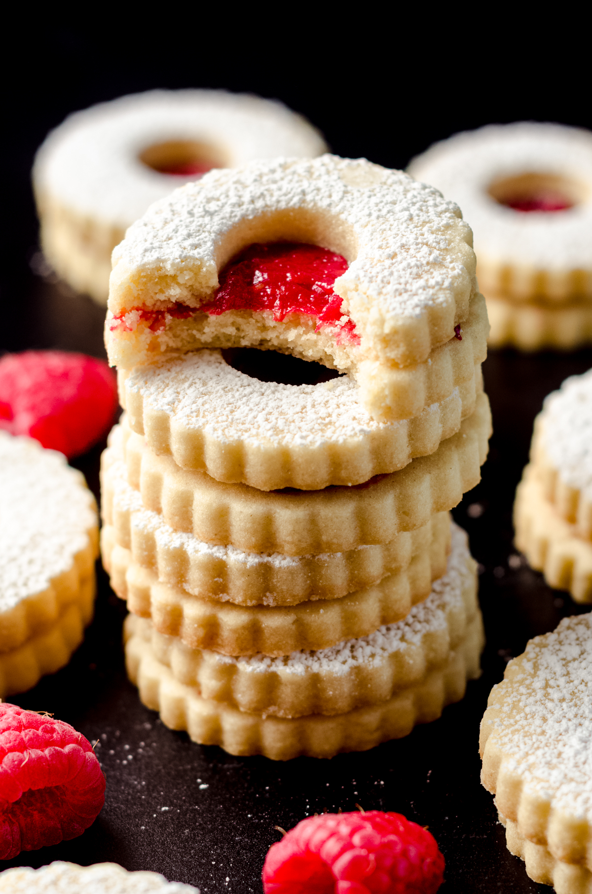 A stack of raspberry Linzer cookies with a bite taken out of the one on top.