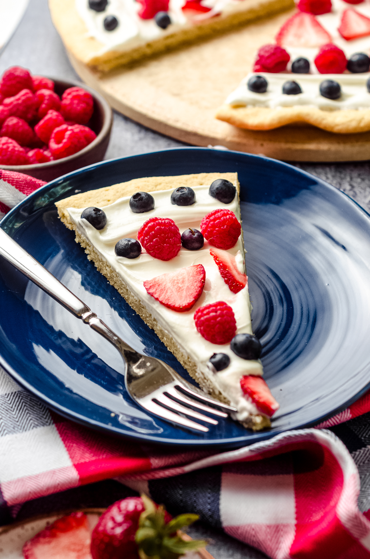 A slice of 4th of July fruit pizza on a blue plate with a fork.