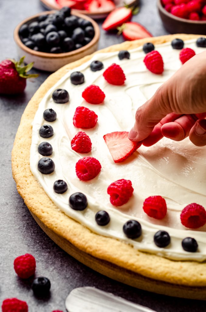 Someone is placing sliced fruit onto a 4th of July fruit pizza.