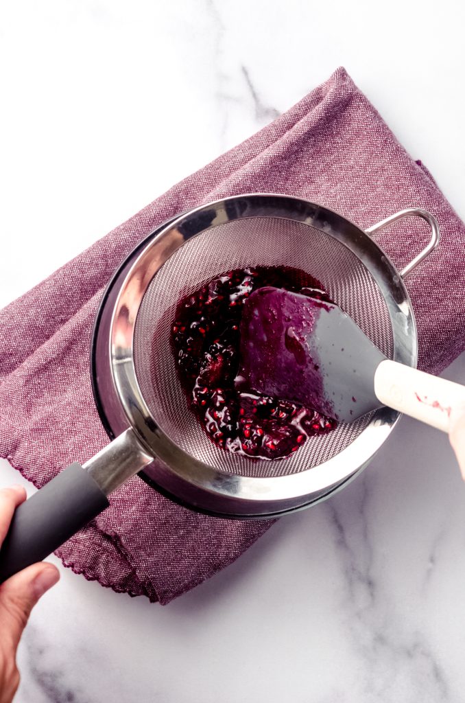 Someone is pressing blackberry puree through a mesh sieve.