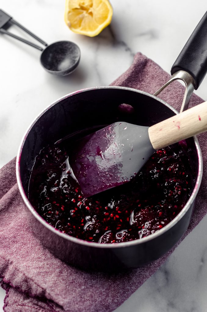 Blackberry puree cooked in a saucepan with a spatula.