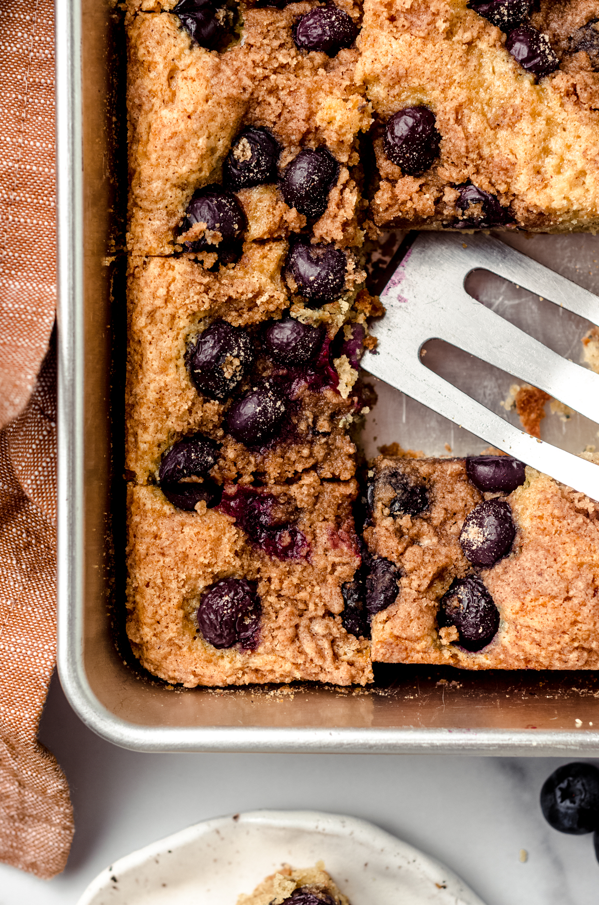 Aerial photo of sliced blueberry coffee cake in a pan with a serving spatula.