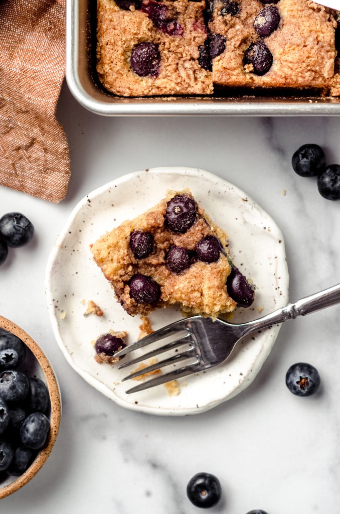 Aerial photo of a slice of blueberry sour cream coffee cake on a plate with a fork.