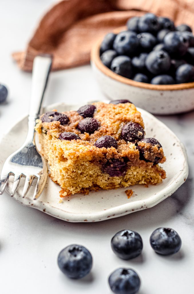 A slice of blueberry sour cream coffee cake on a plate with a fork.