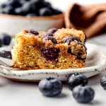 A slice of blueberry sour cream coffee cake on a plate with a fork.