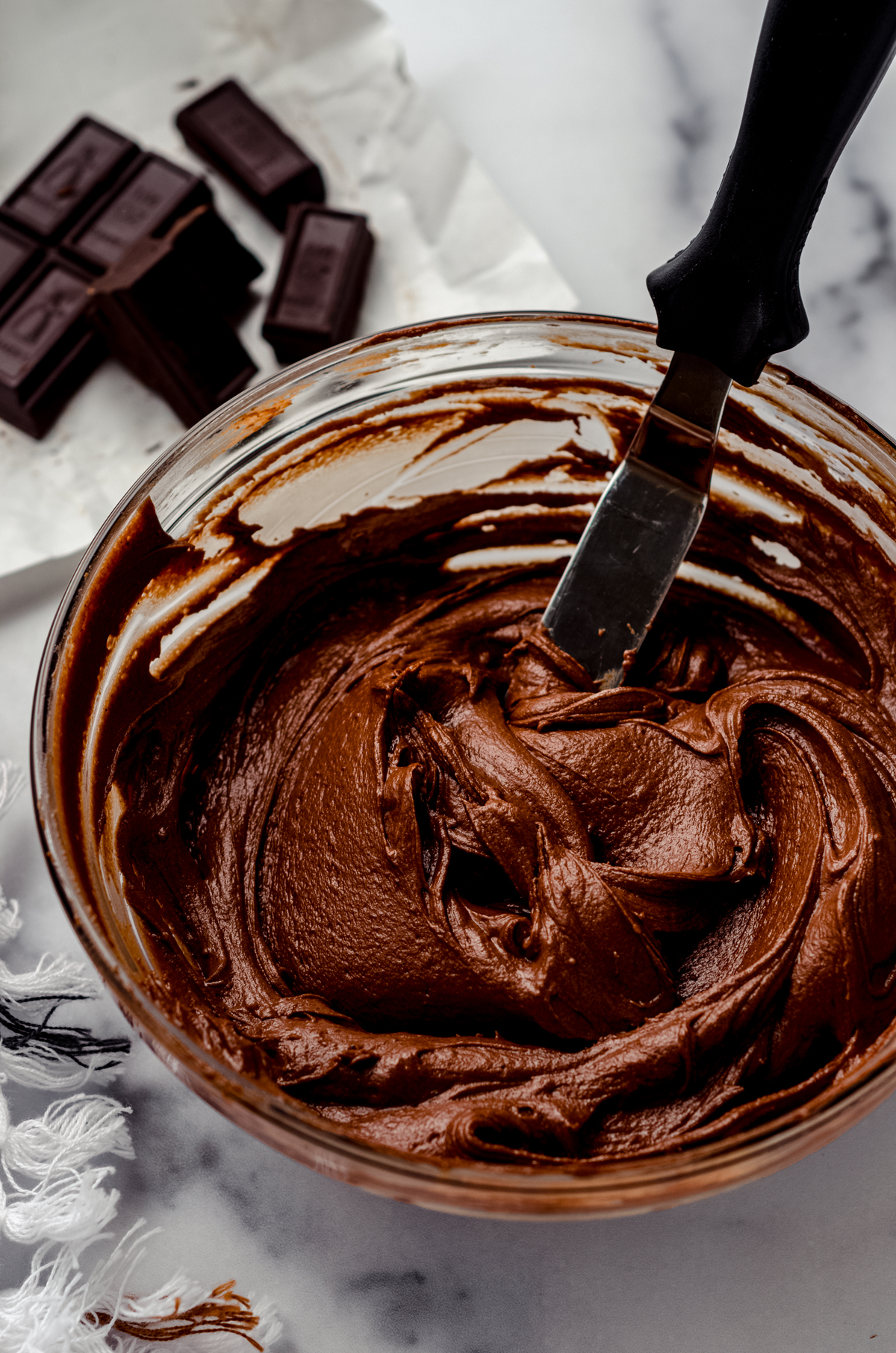 A bowl of chocolate fudge frosting with a spatula in it.
