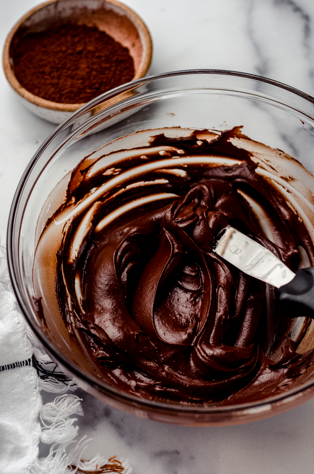 A bowl of chocolate frosting made with cocoa powder in a bowl with a spatula.