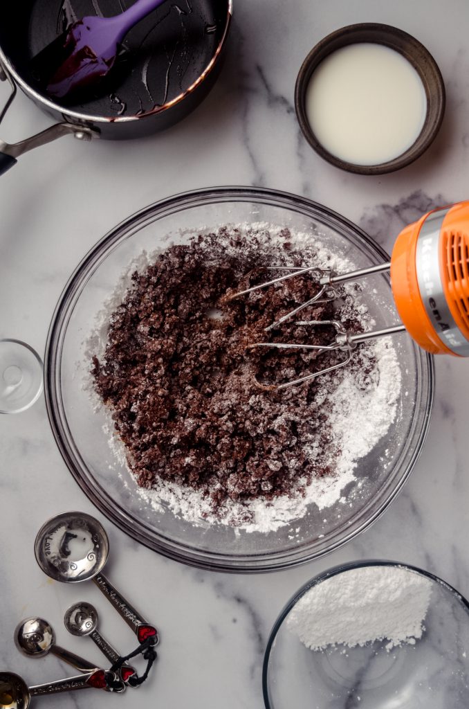 Aerial photo of ingredients in a bowl being mixed with a hand mixer to make chocolate fudge frosting.