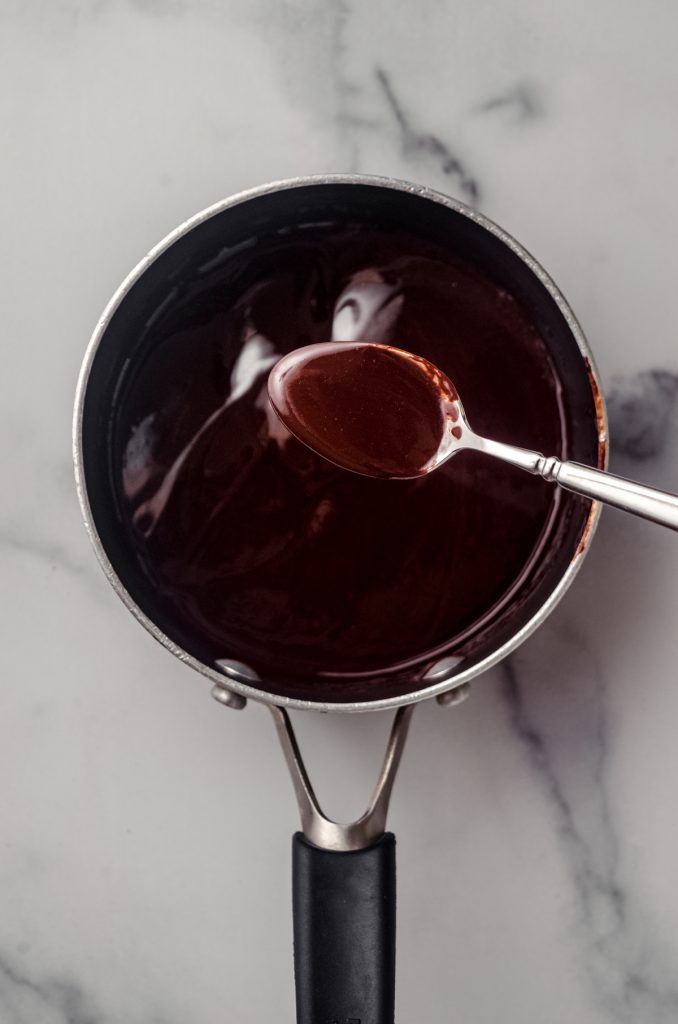 Someone is using a spoon to lift melted chocolate mixture out of a saucepan.