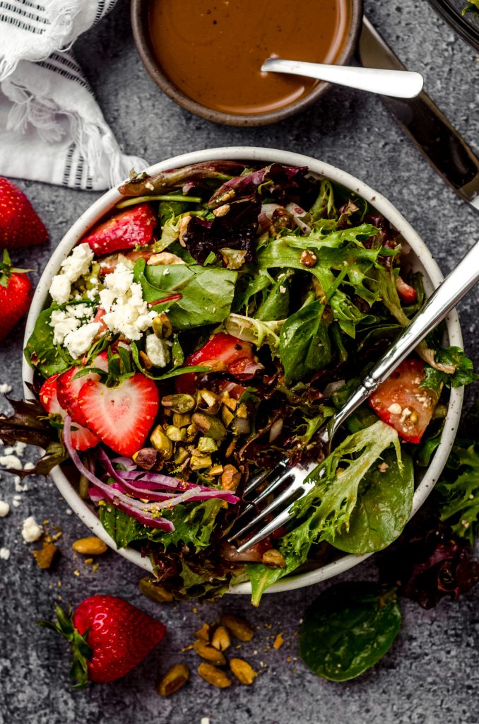 A bowl of strawberry spinach salad with a fork in it.