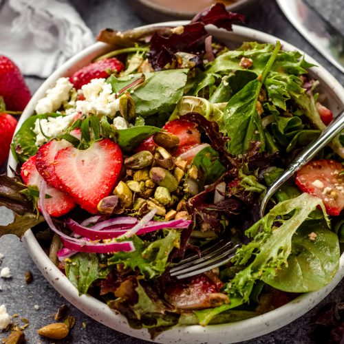 A bowl of strawberry spinach salad with a fork in it.