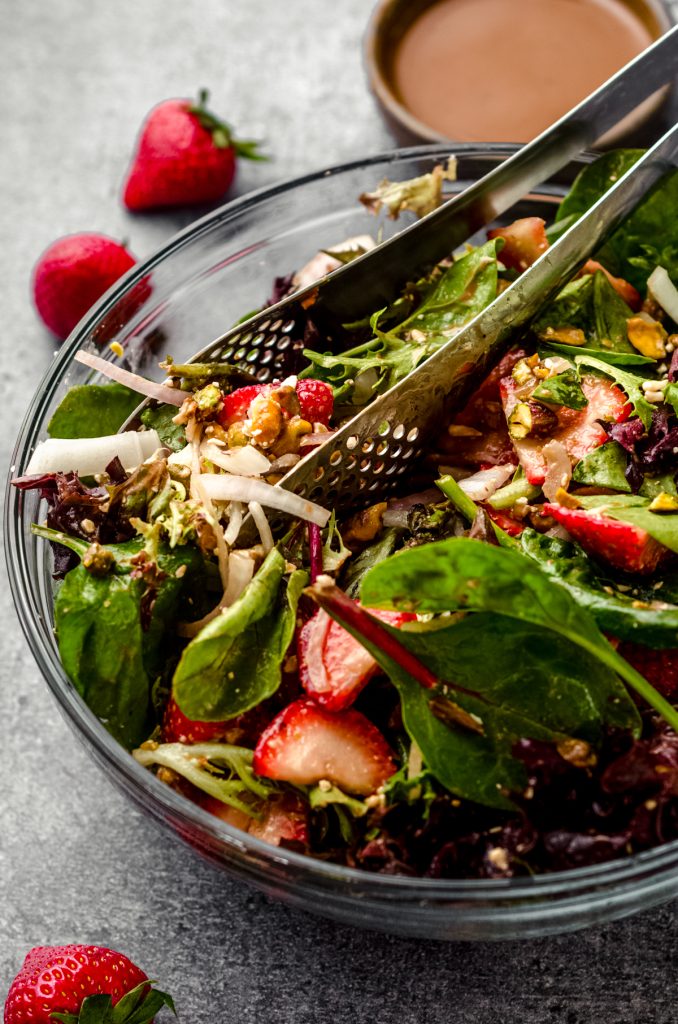 Tossed strawberry spinach salad with feta in a bowl with metal tongs.