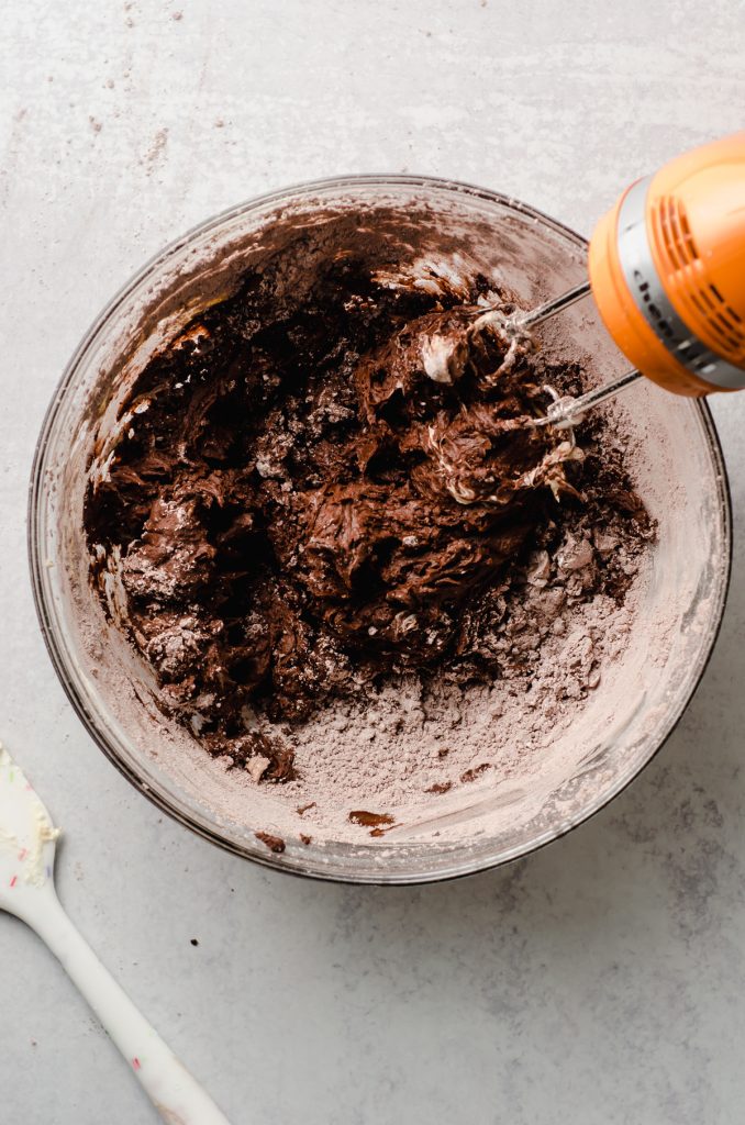 Chocolate frosting being mixed in a bowl with an electric mixer.