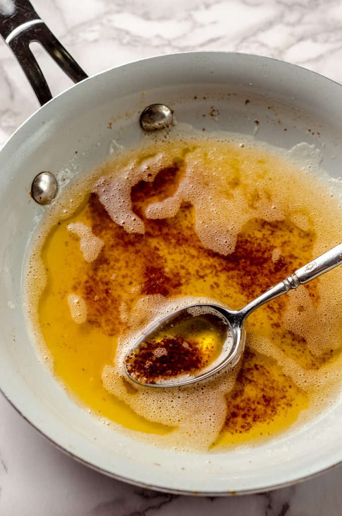 A skillet with brown butter in it. There is a spoon holding some of the cooked milk proteins.
