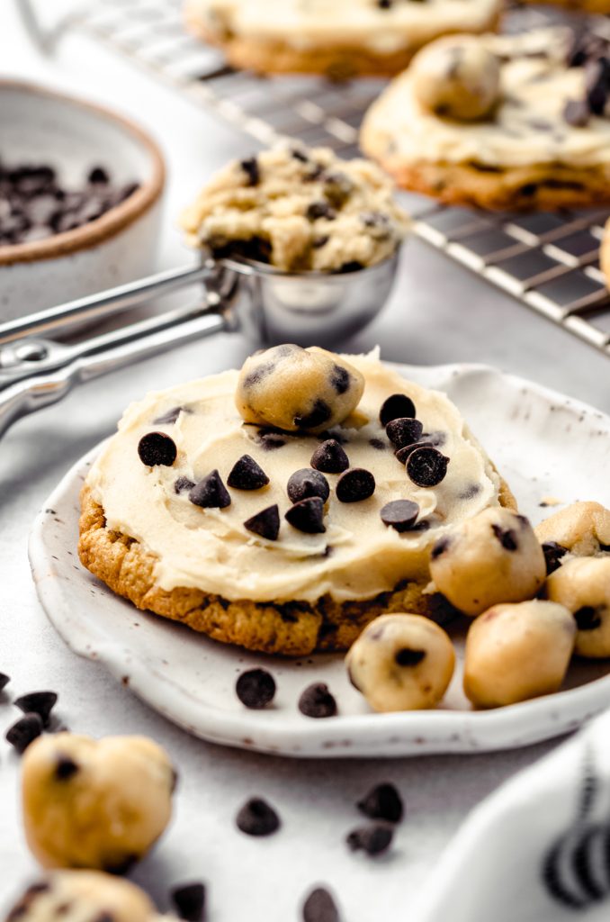 A cookie dough cookie on a plate with edible cookie dough balls and chocolate chips scattered around it.