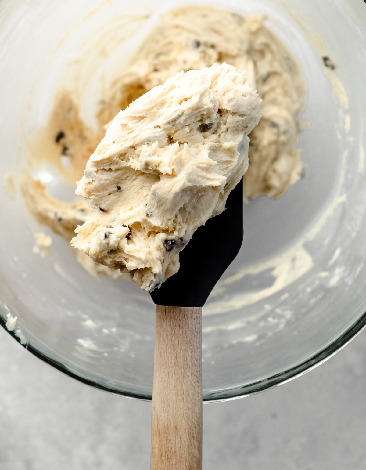 Cookie dough frosting on a spatula being held above a glass bowl.