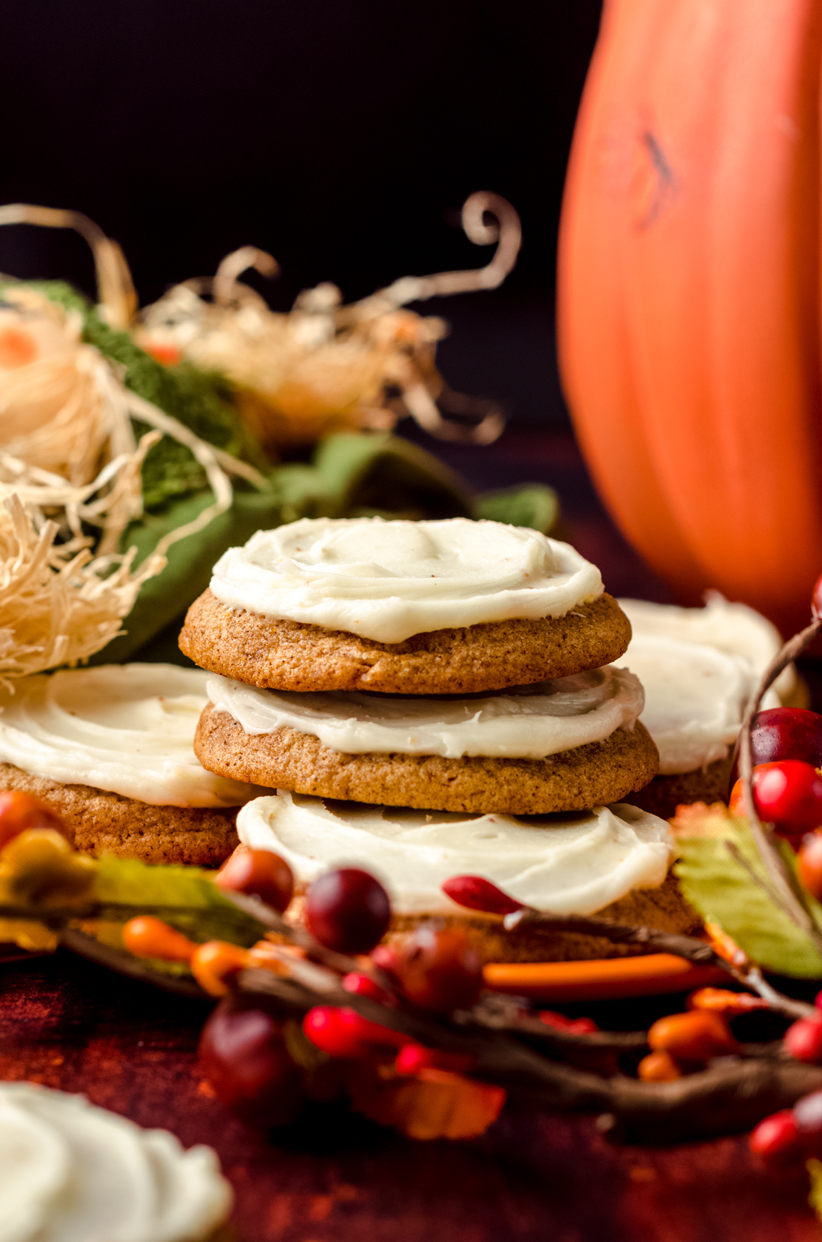 A stack of frosted pumpkin cookies on a plate with fall decor all around.